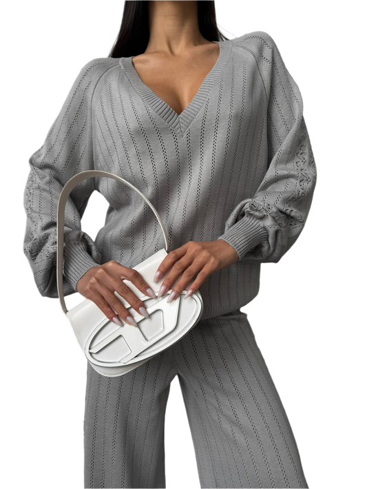 Person wearing a gray ribbed sweater and pants holding a white handbag.