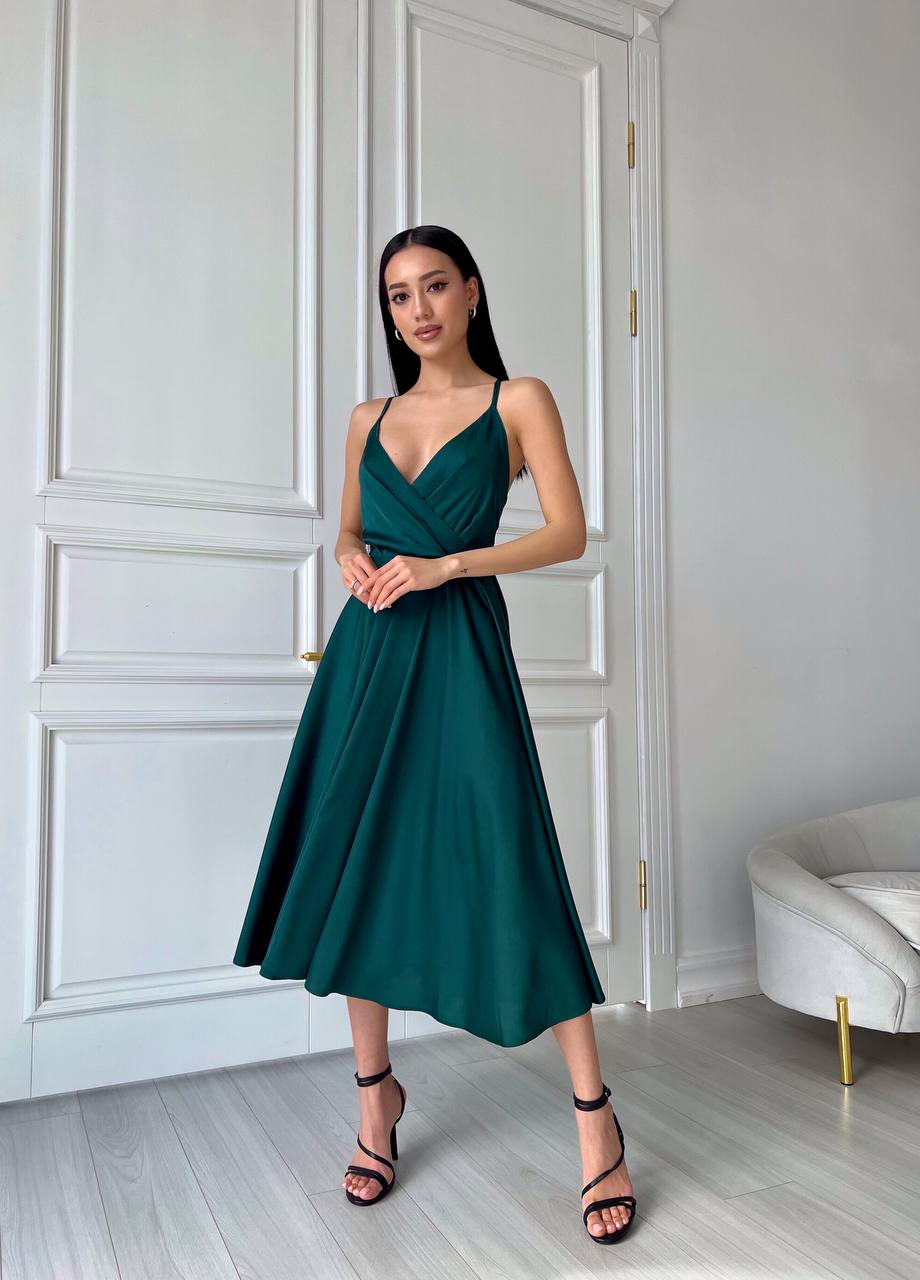 Woman in a teal dress standing in a room with white paneled walls and a white sofa.