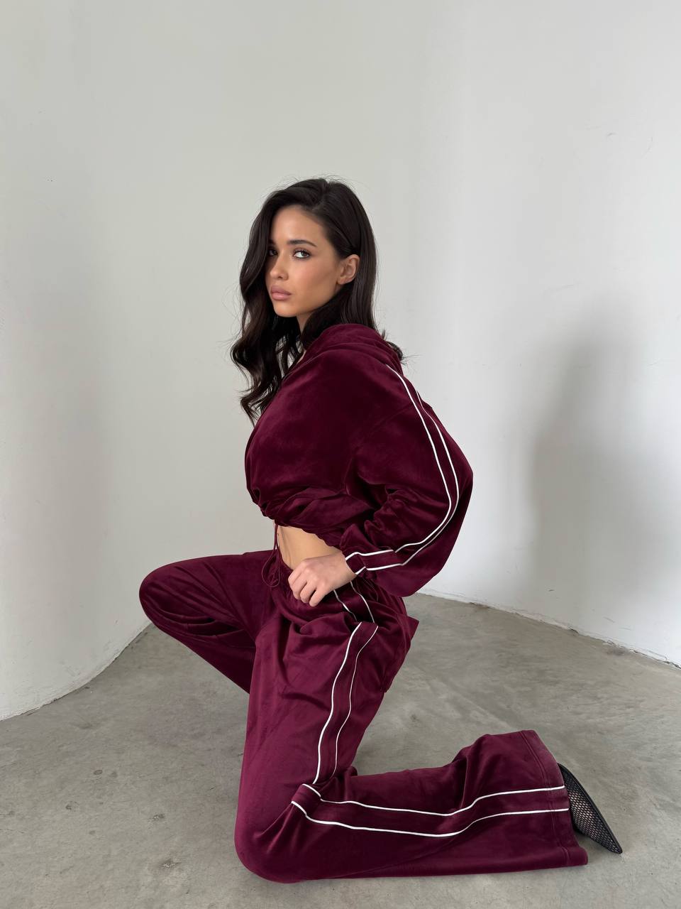 Woman wearing a burgundy tracksuit with white piping on a plain background