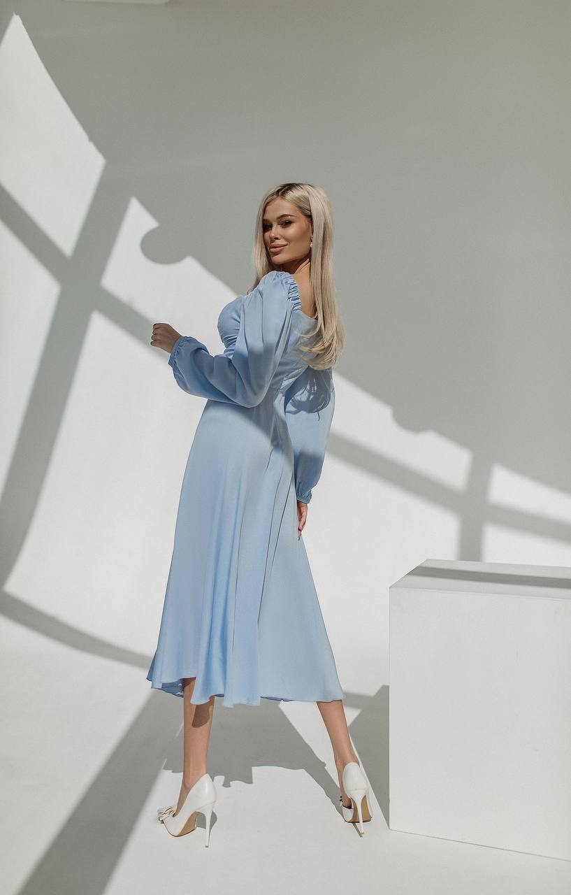 Woman in a light blue dress standing against a white wall with shadows.