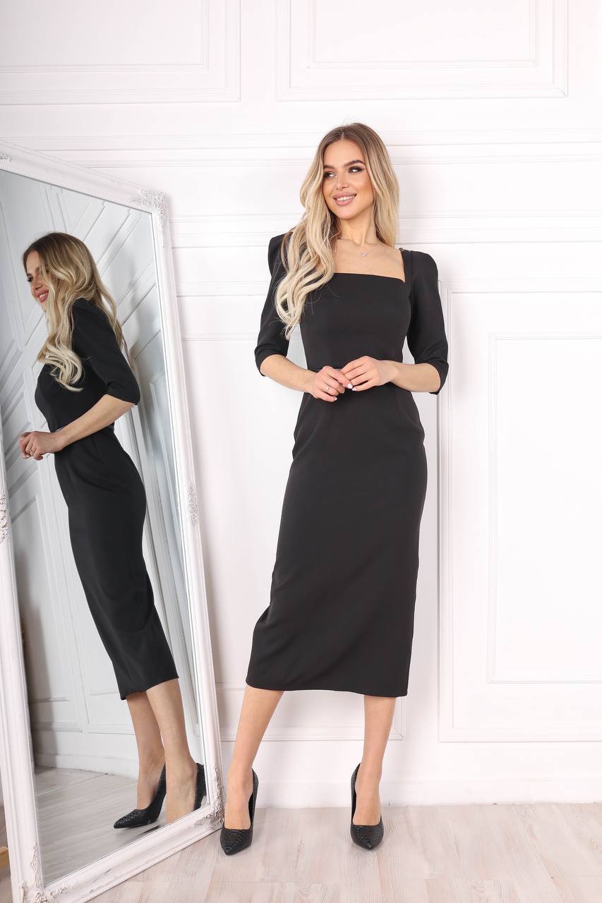 Woman wearing a black dress standing in front of a mirror.