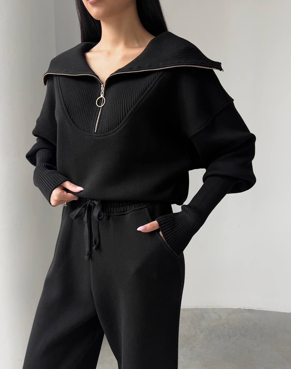 Person wearing a black outfit with a high collar and drawstring pants against a plain background