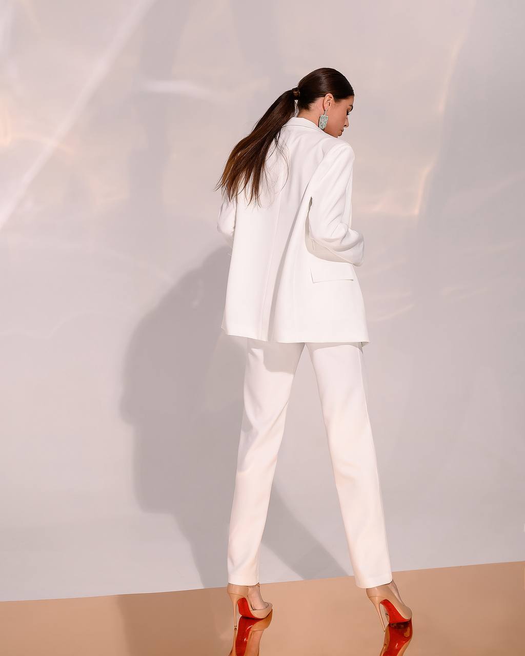 Woman in a white suit standing against a plain background