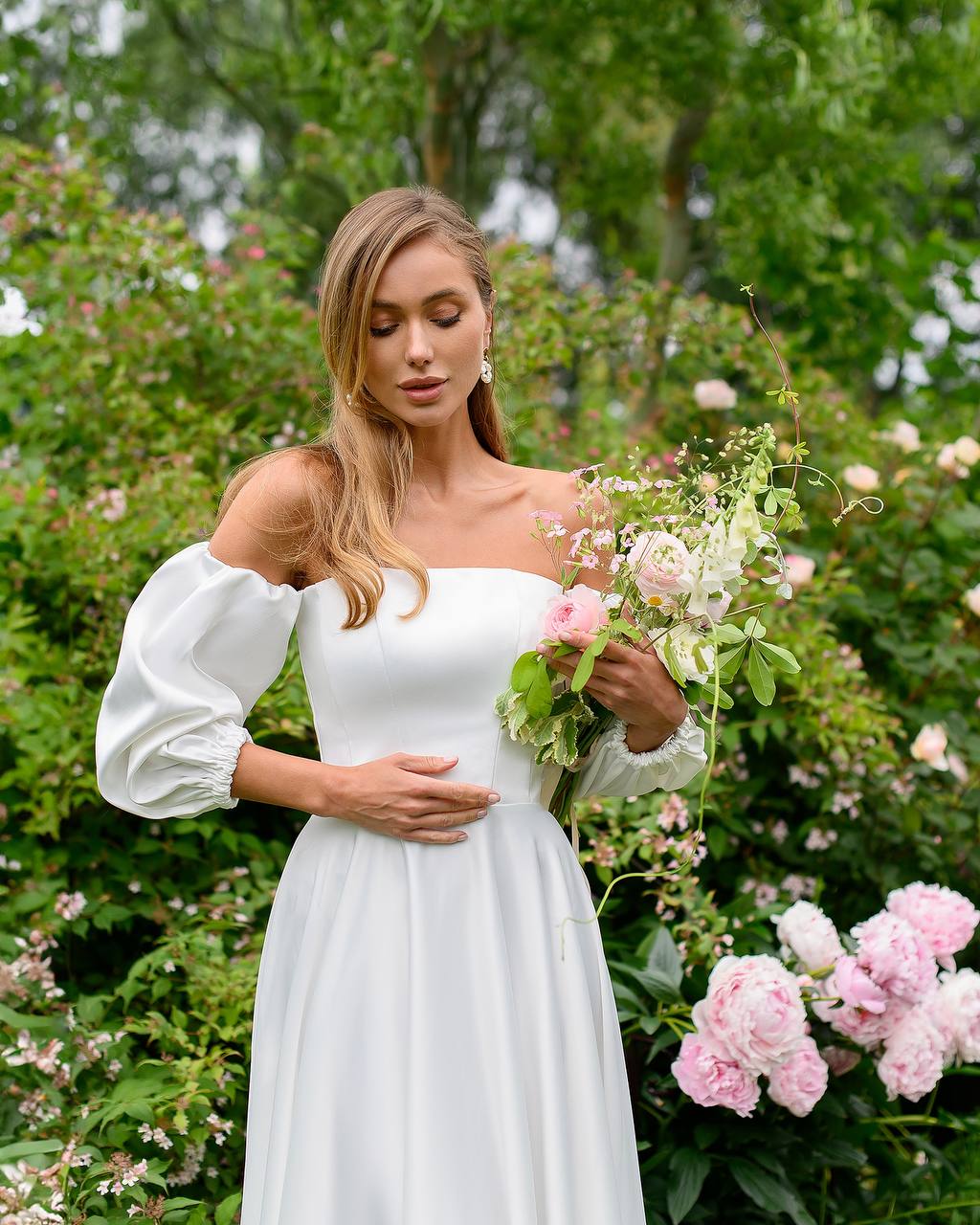 Woman in a white dress holding flowers in a garden setting