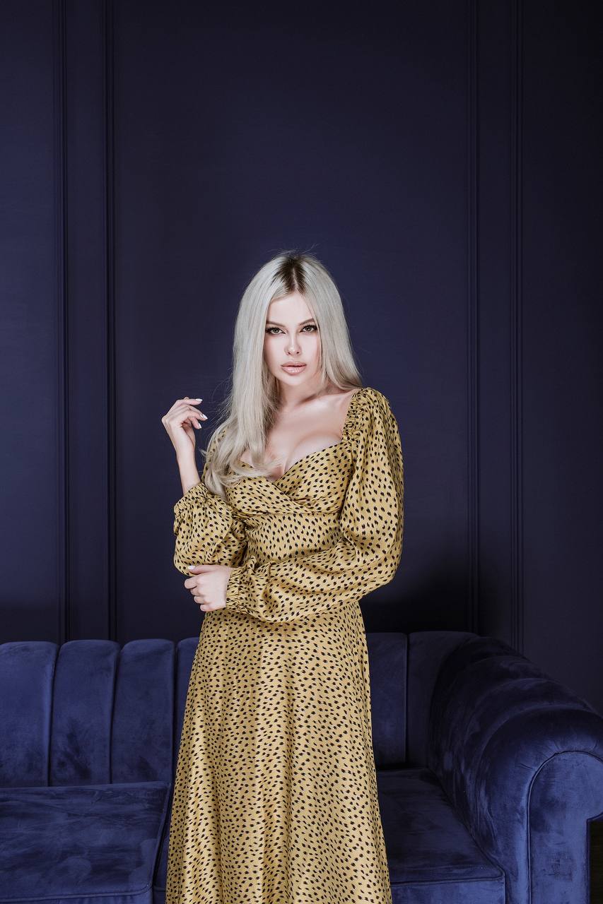 Woman in a gold dress standing against a dark blue wall with a blue couch.