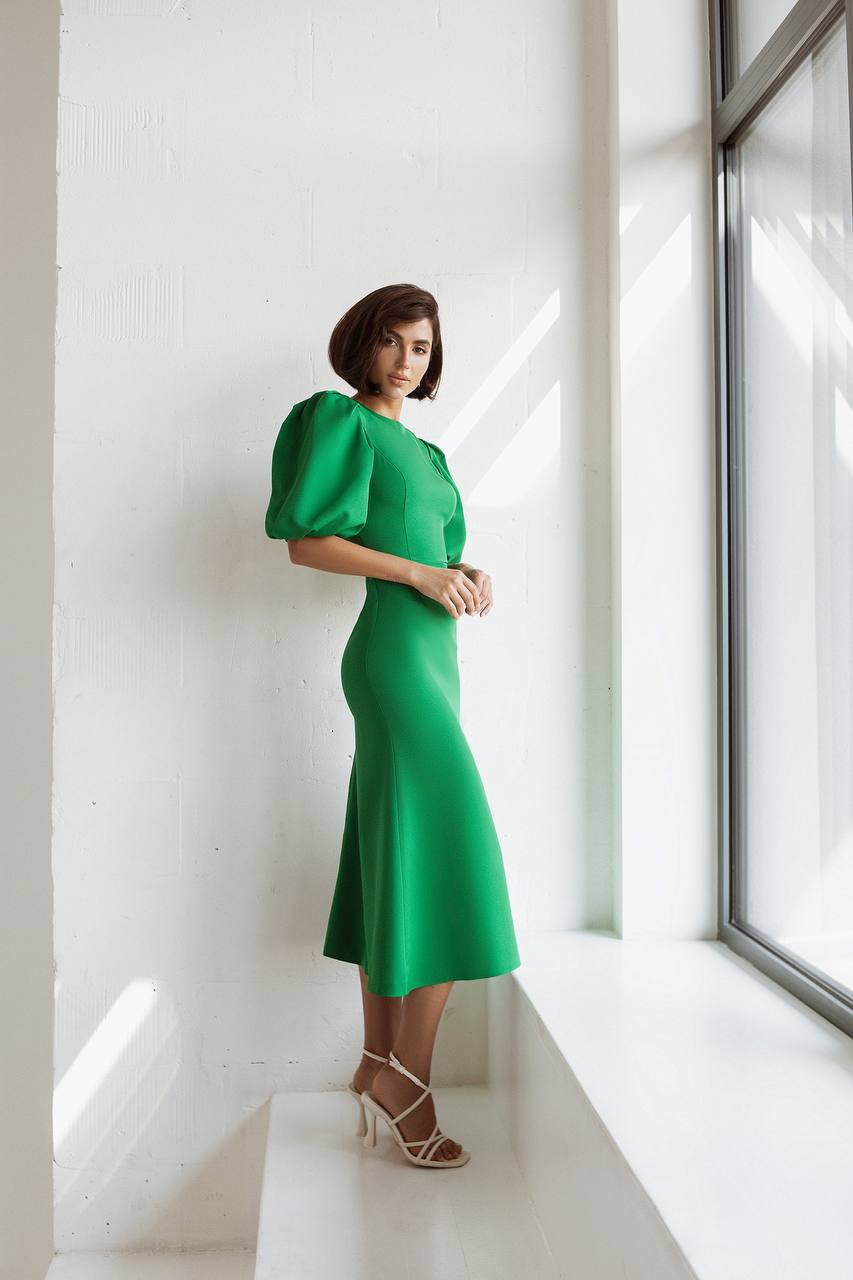 Woman in a green dress standing by a window in a bright room
