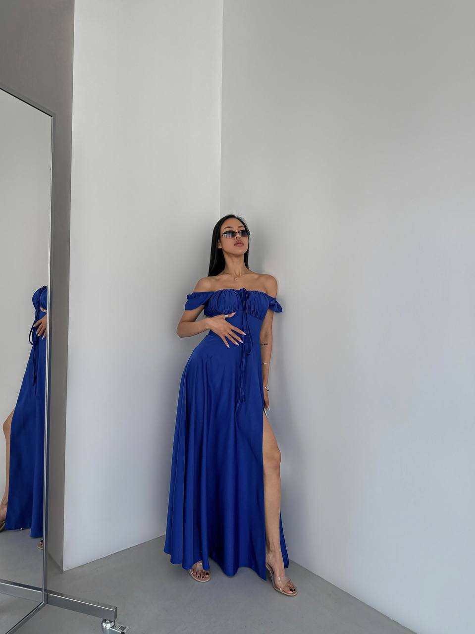 Woman in a blue off-shoulder gown standing in a minimalistic room.