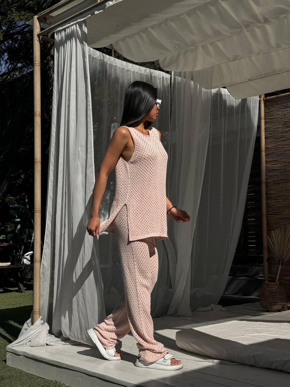 Woman in a pink knitted outfit standing in front of a white curtain
