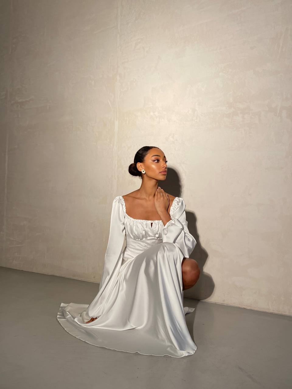 Woman in a white dress sitting against a plain wall