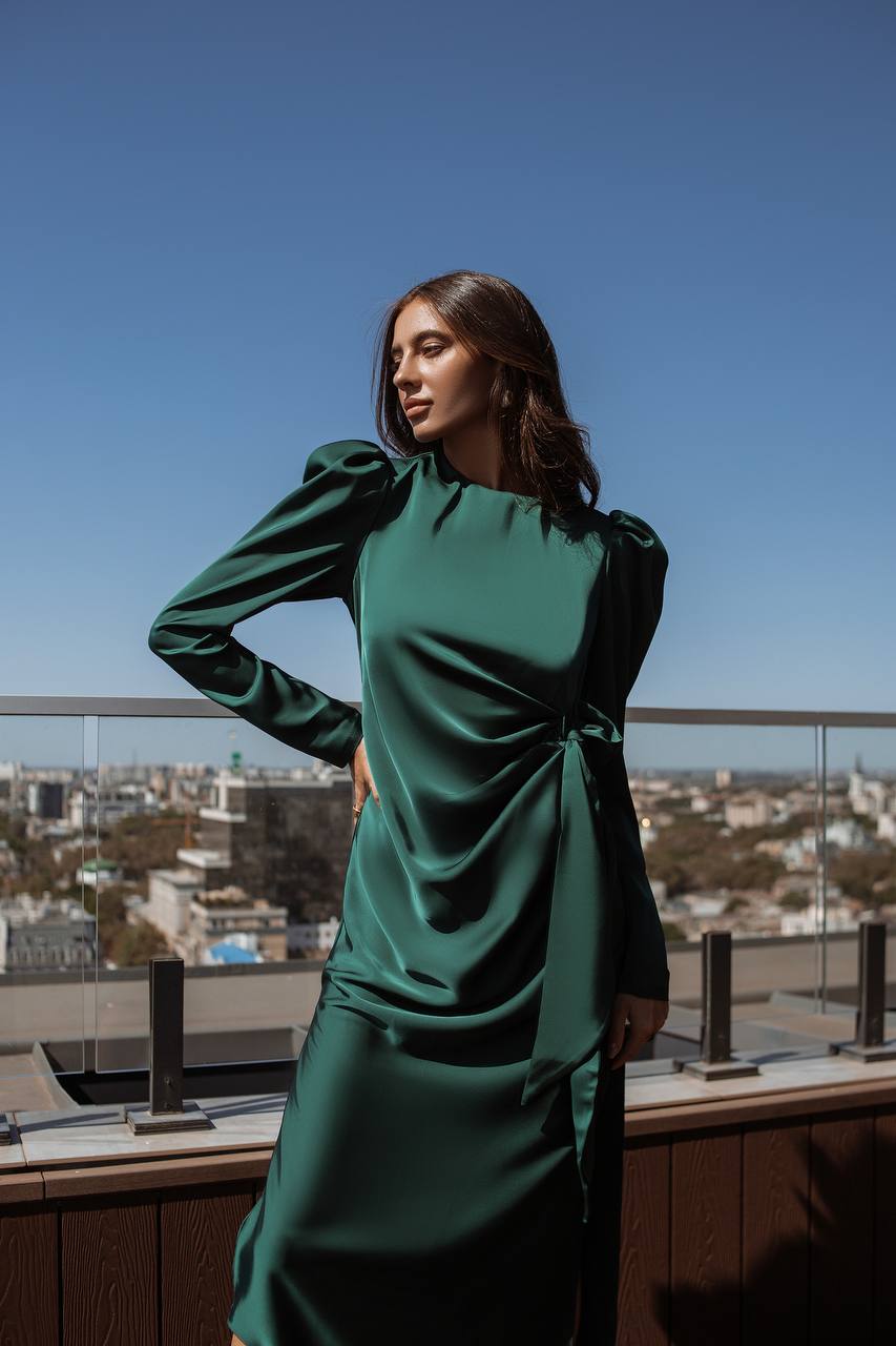 Woman in a green dress standing on a rooftop with a cityscape in the background