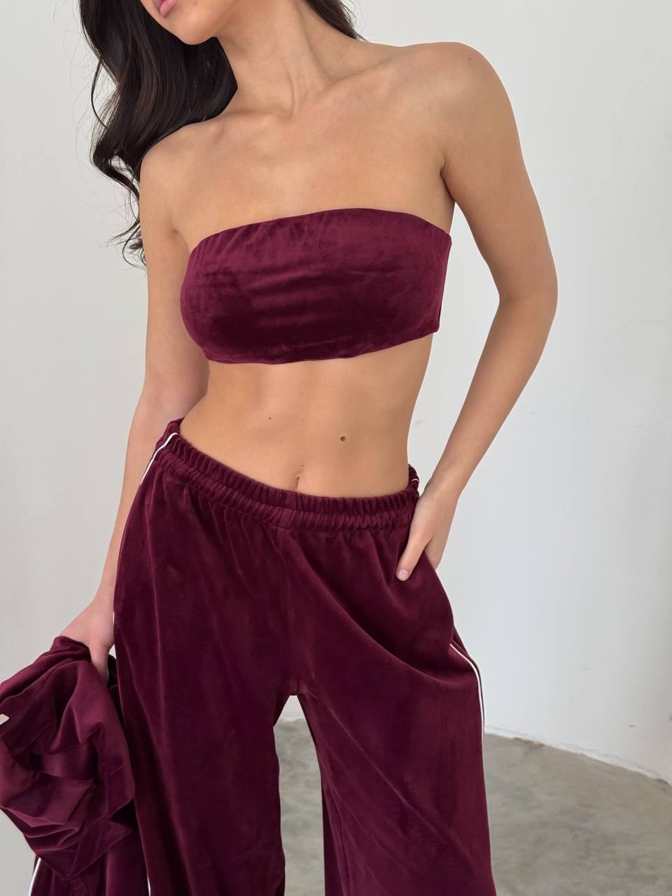 Woman wearing a burgundy strapless top and wide-leg pants against a white background