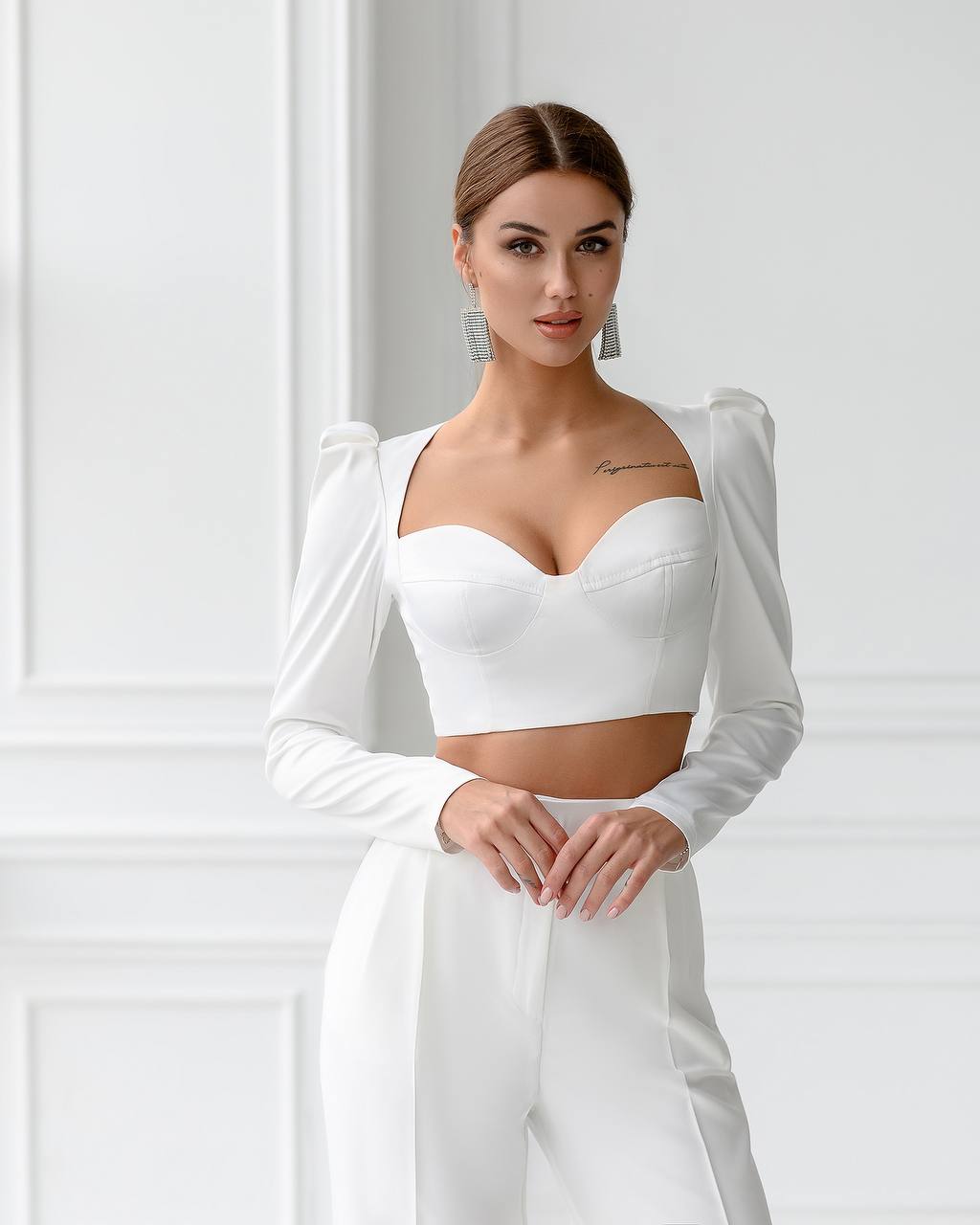 Woman wearing a white outfit with long sleeves against a white wall