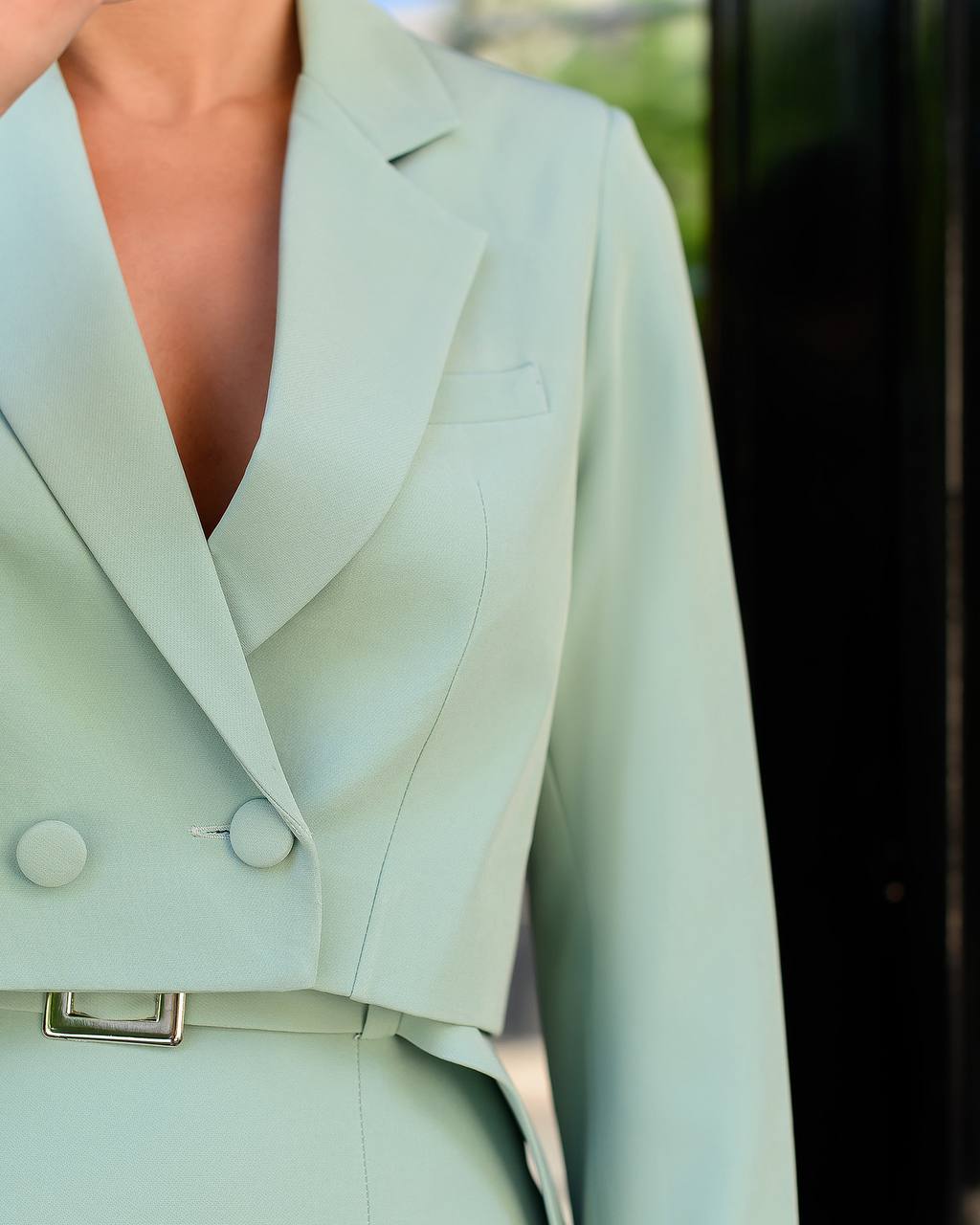 Light green blazer with a belt against a blurred outdoor background