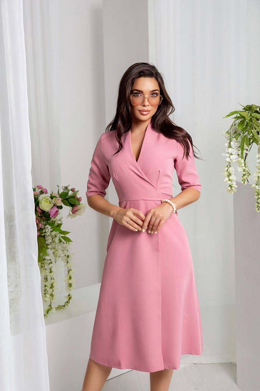 Woman wearing a pink dress standing against a white curtain background