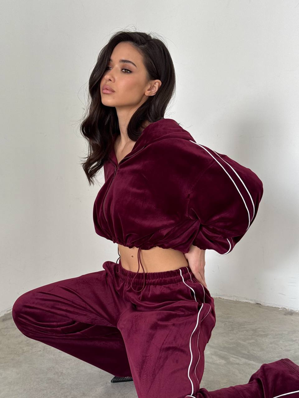 Woman wearing a burgundy tracksuit with white stripes on a plain background