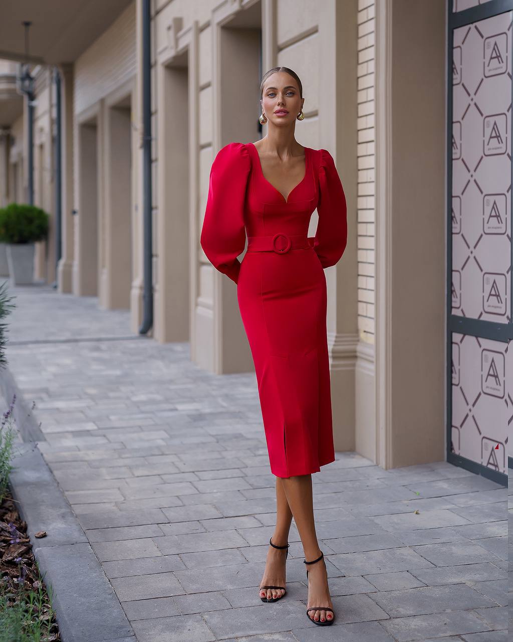 Woman in a red dress standing on a sidewalk with a building in the background