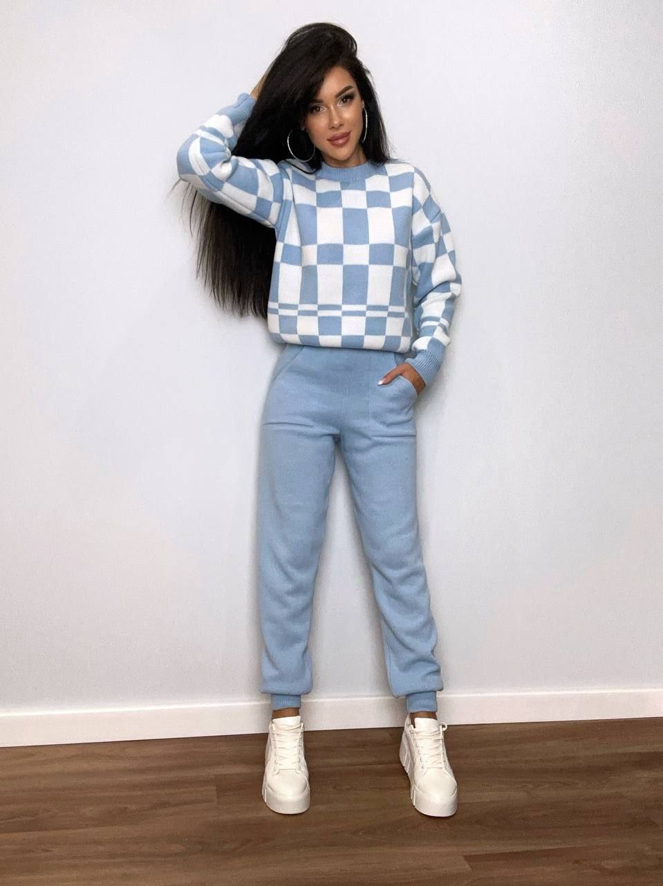 Woman wearing a blue and white checkered sweater and matching pants against a white wall.