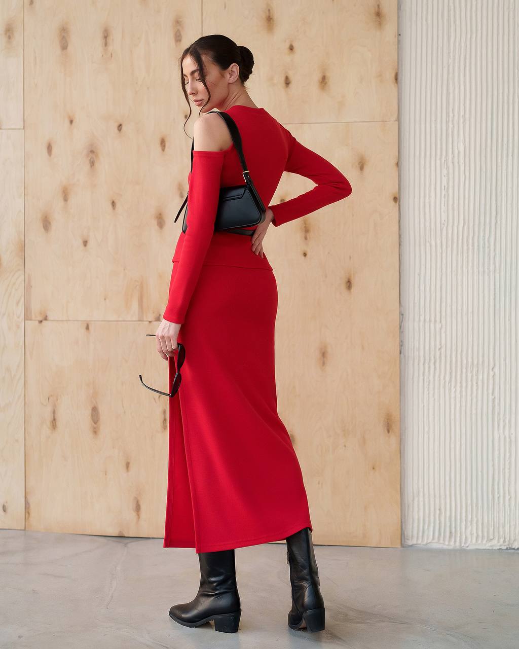 Woman in a red dress with black boots standing against a wooden wall.