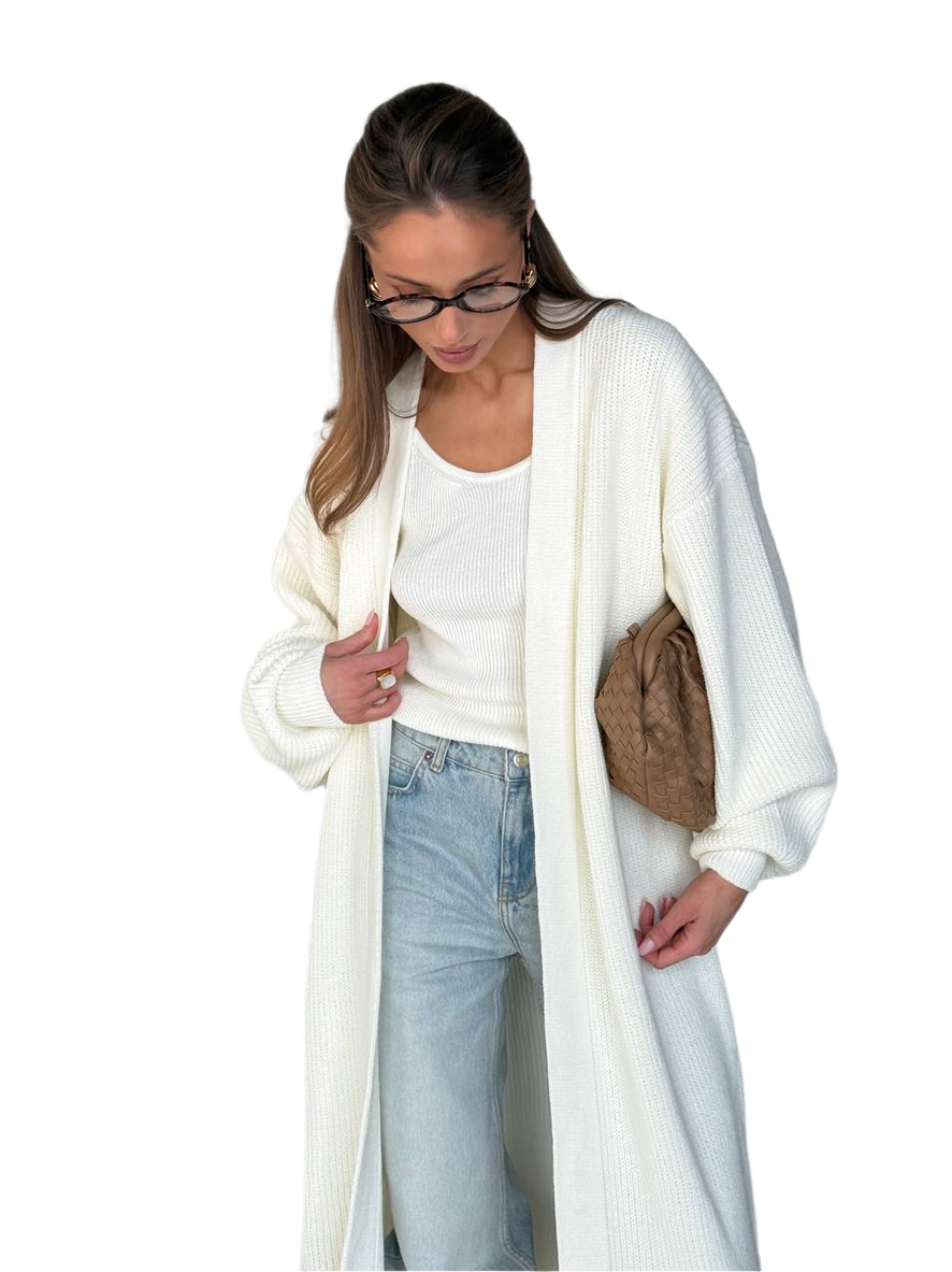 Woman wearing a long cream cardigan over a white top and blue jeans, holding a brown bag on a white background.