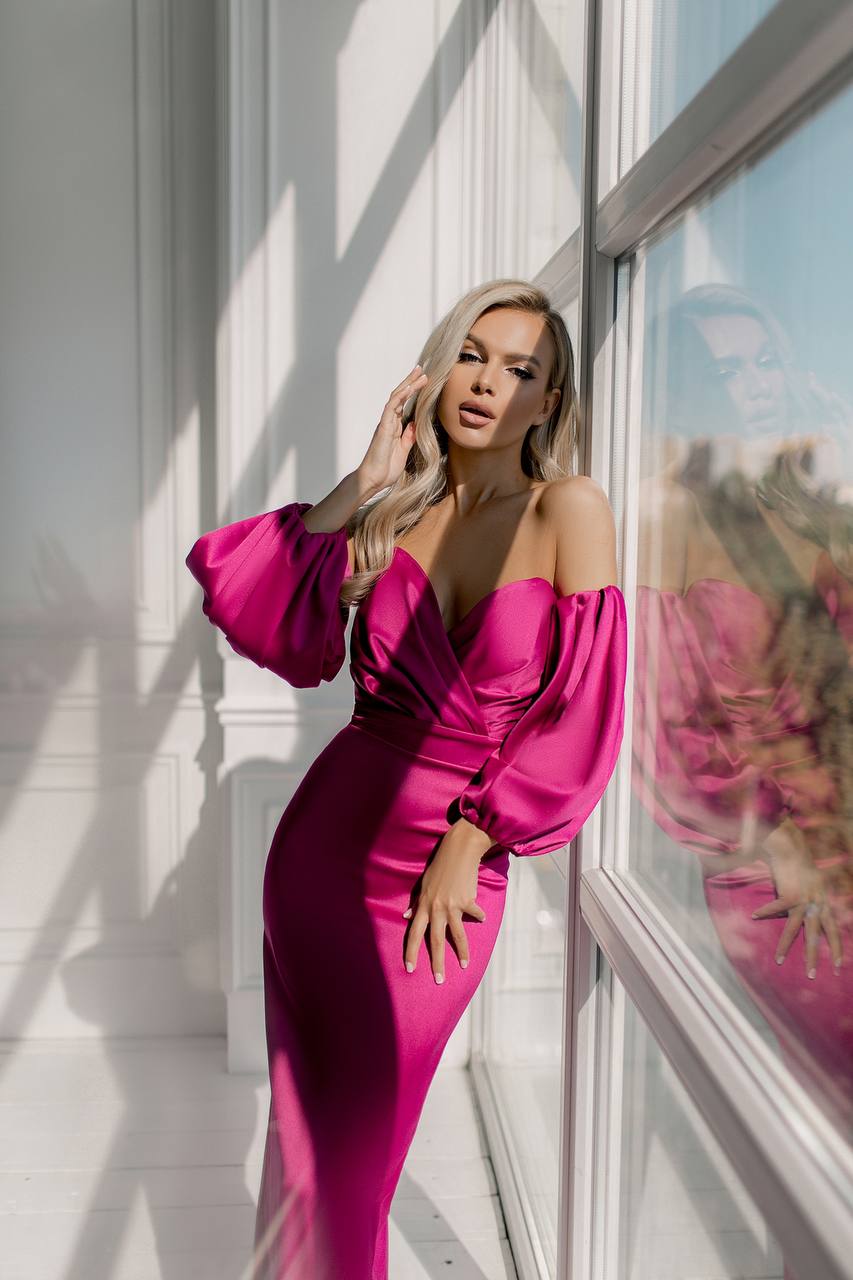 Woman in a pink dress standing by a window with a scenic view.