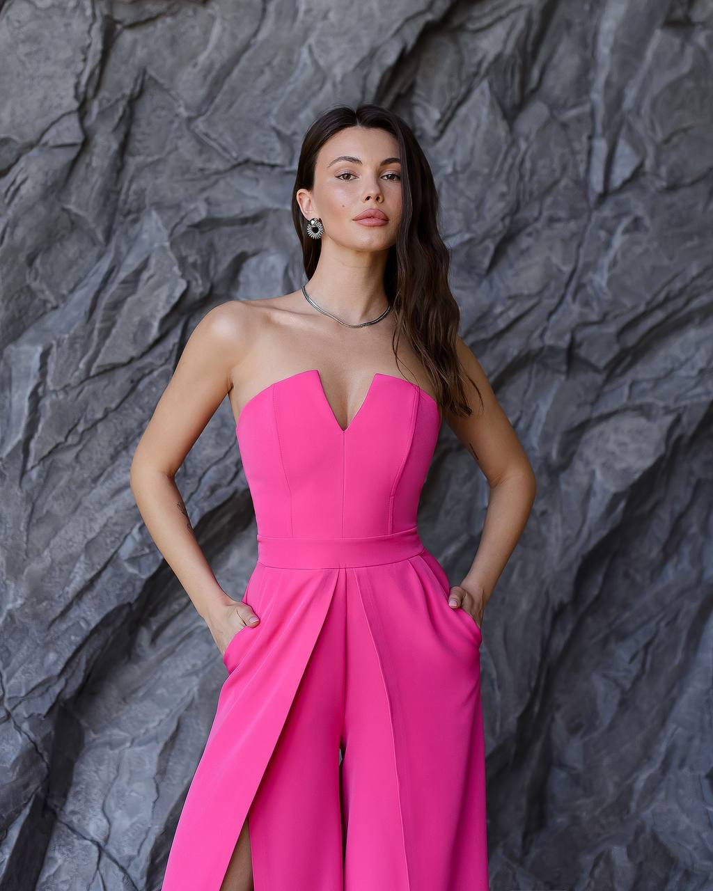 Woman wearing a pink strapless jumpsuit against a textured gray background