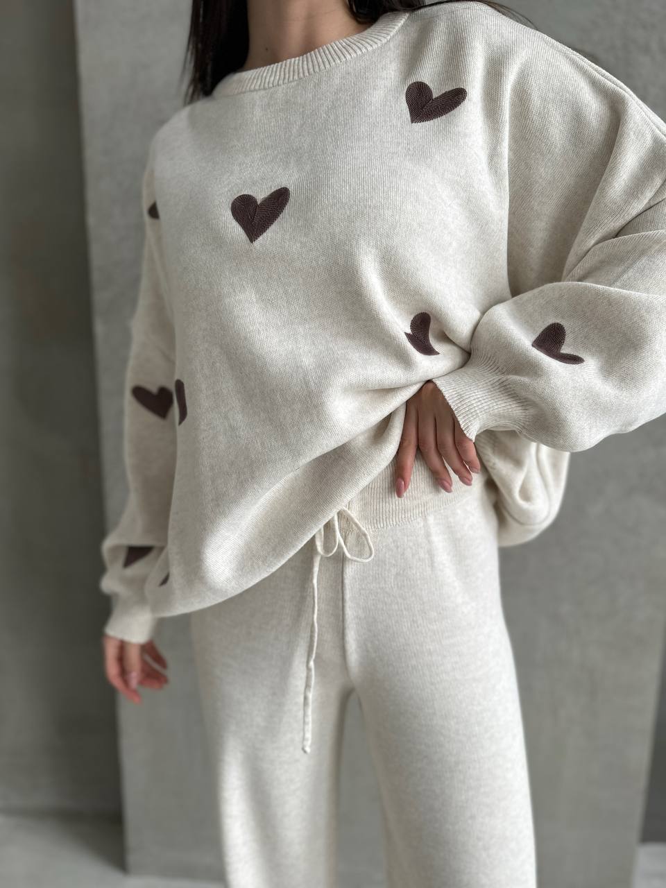 Person wearing a white sweater with brown heart patterns and matching pants against a neutral background