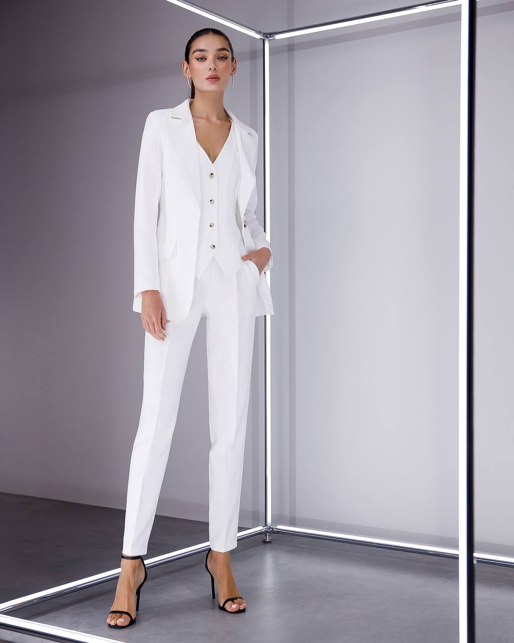 Woman wearing a white suit standing in a modern, minimalistic room.