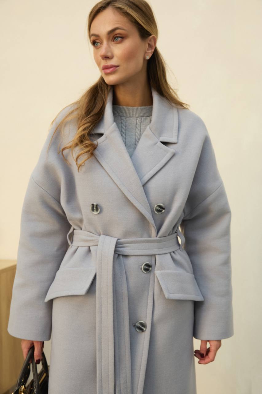 Woman wearing a light blue coat with a belt against a neutral background