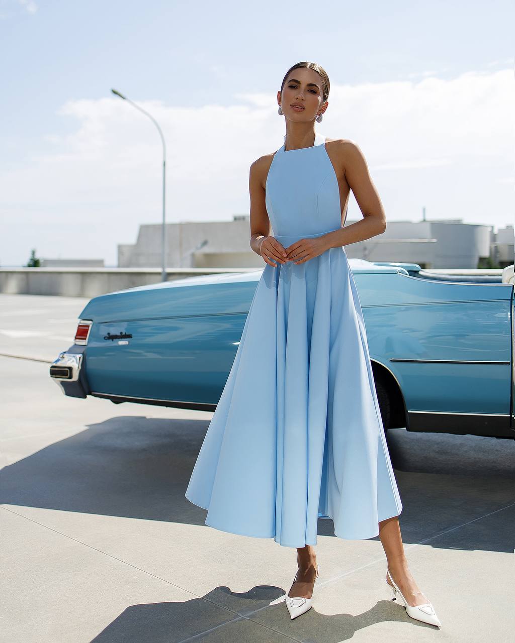 Woman in a light blue dress standing next to a vintage blue car.