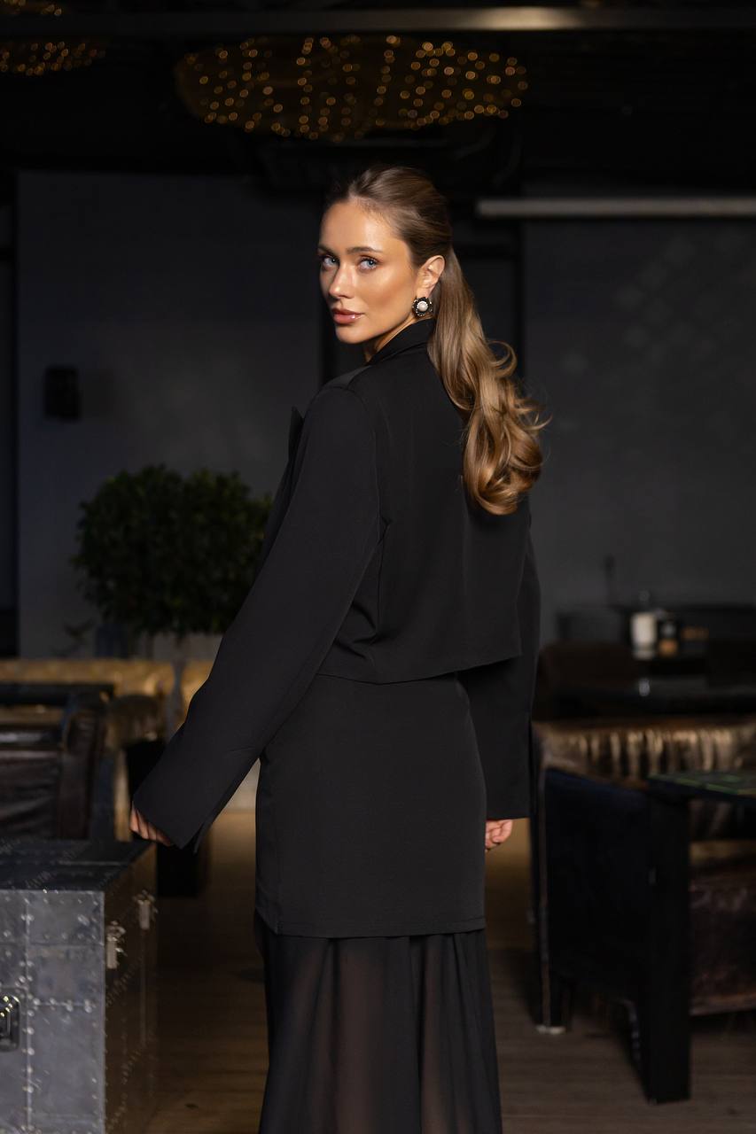 Woman in a black outfit standing in a dimly lit room with dark decor.