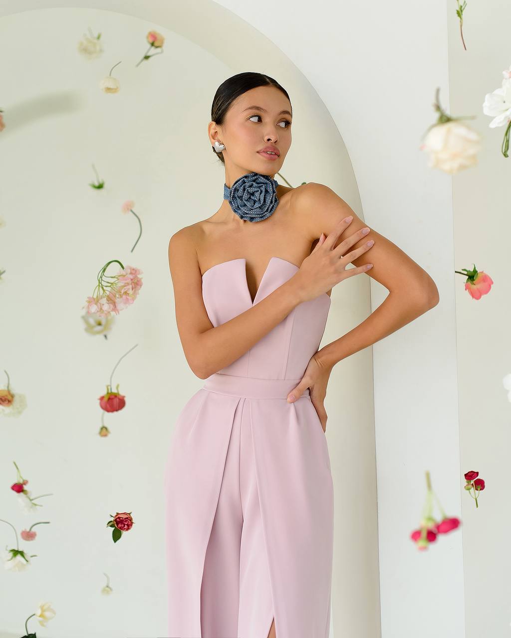 Woman wearing a strapless pink jumpsuit with floral decorations in the background