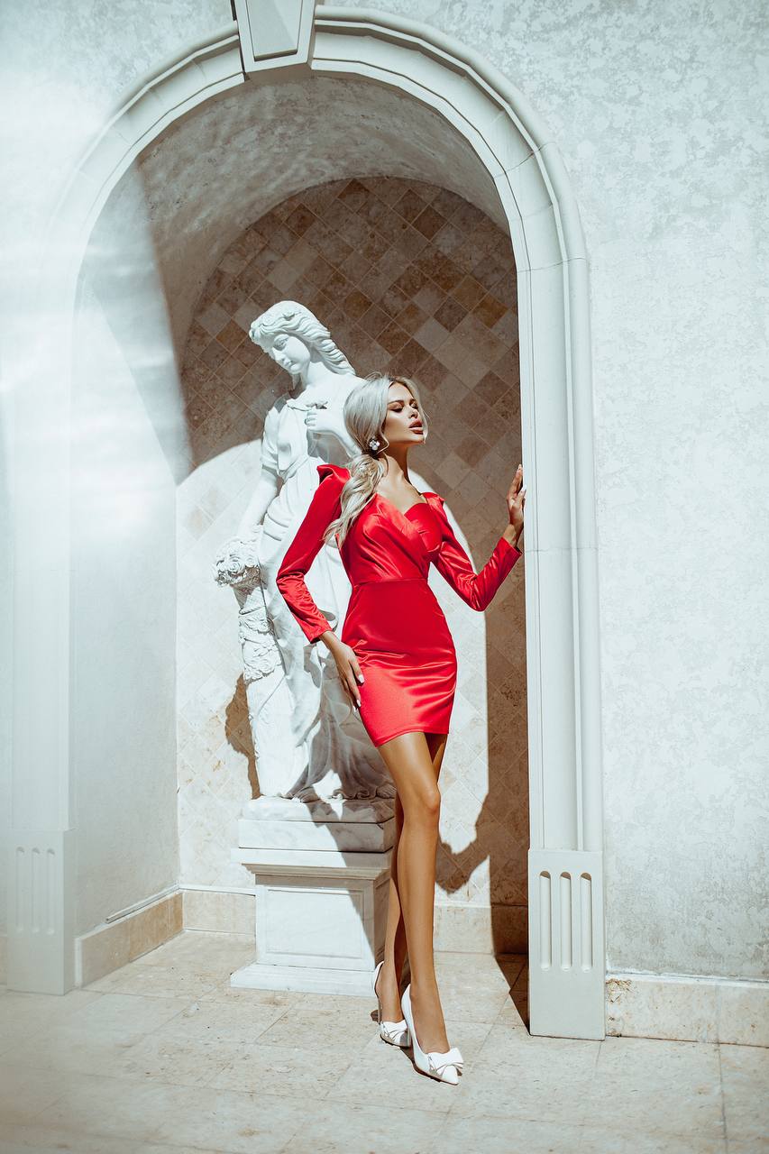 Woman in a red dress standing next to a marble statue in an elegant setting