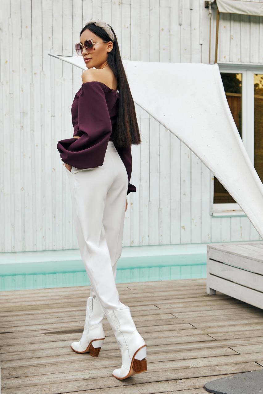 Woman in burgundy top and white pants standing on a wooden deck by a pool.