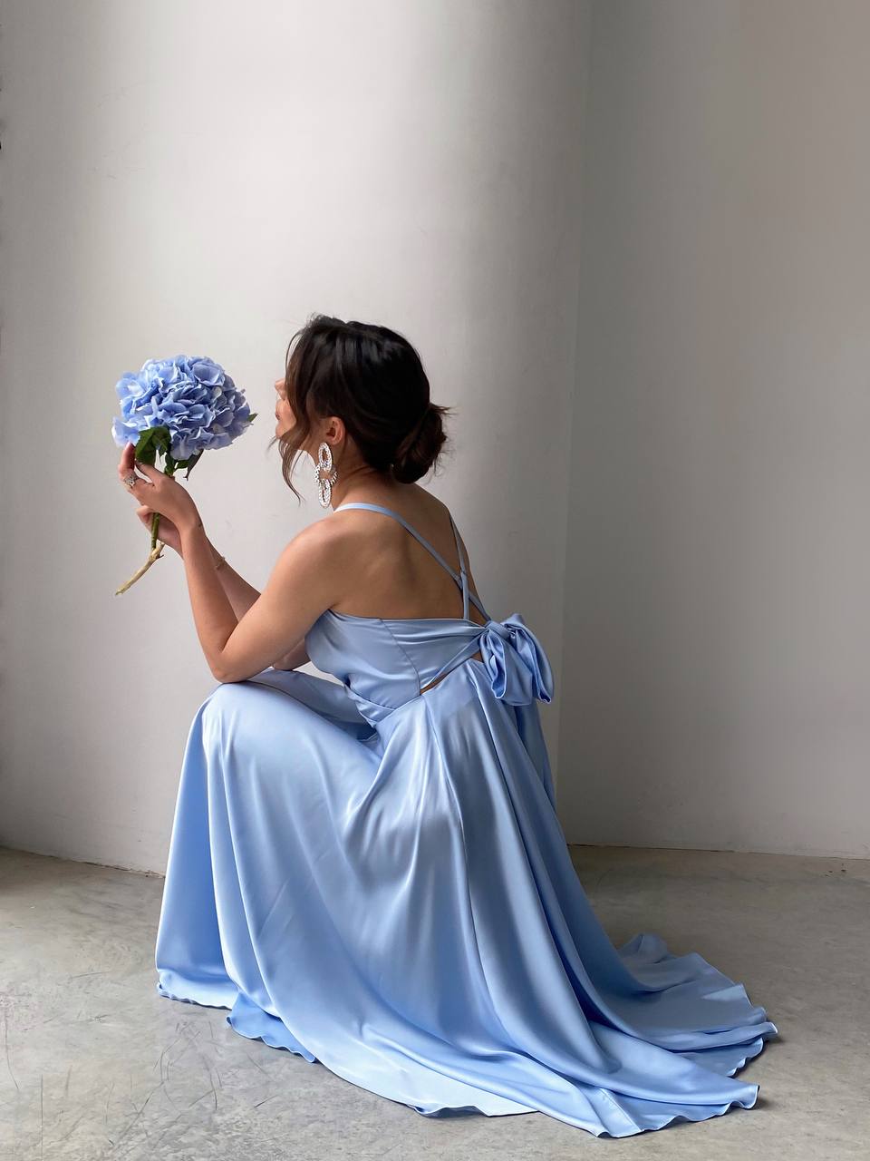 Woman in a light blue dress holding a bouquet of flowers against a plain background