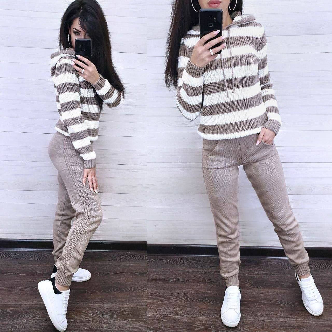 Woman wearing a striped sweater and beige pants against a white wall.