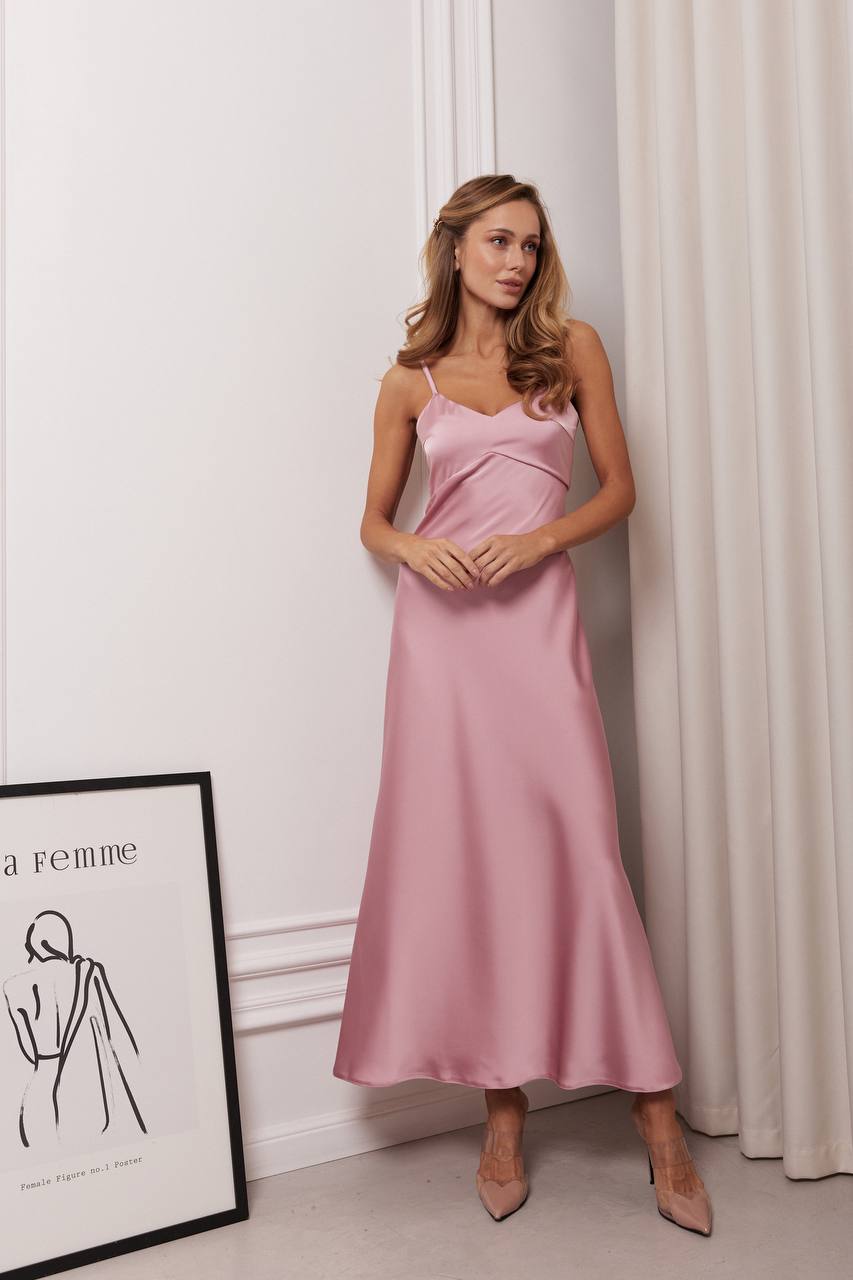 Woman wearing a pink dress standing against a white wall with a framed picture on the floor.