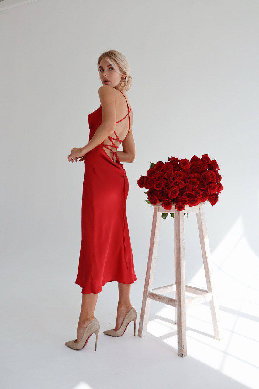 Woman in a red dress standing next to a stool with red roses on a white background