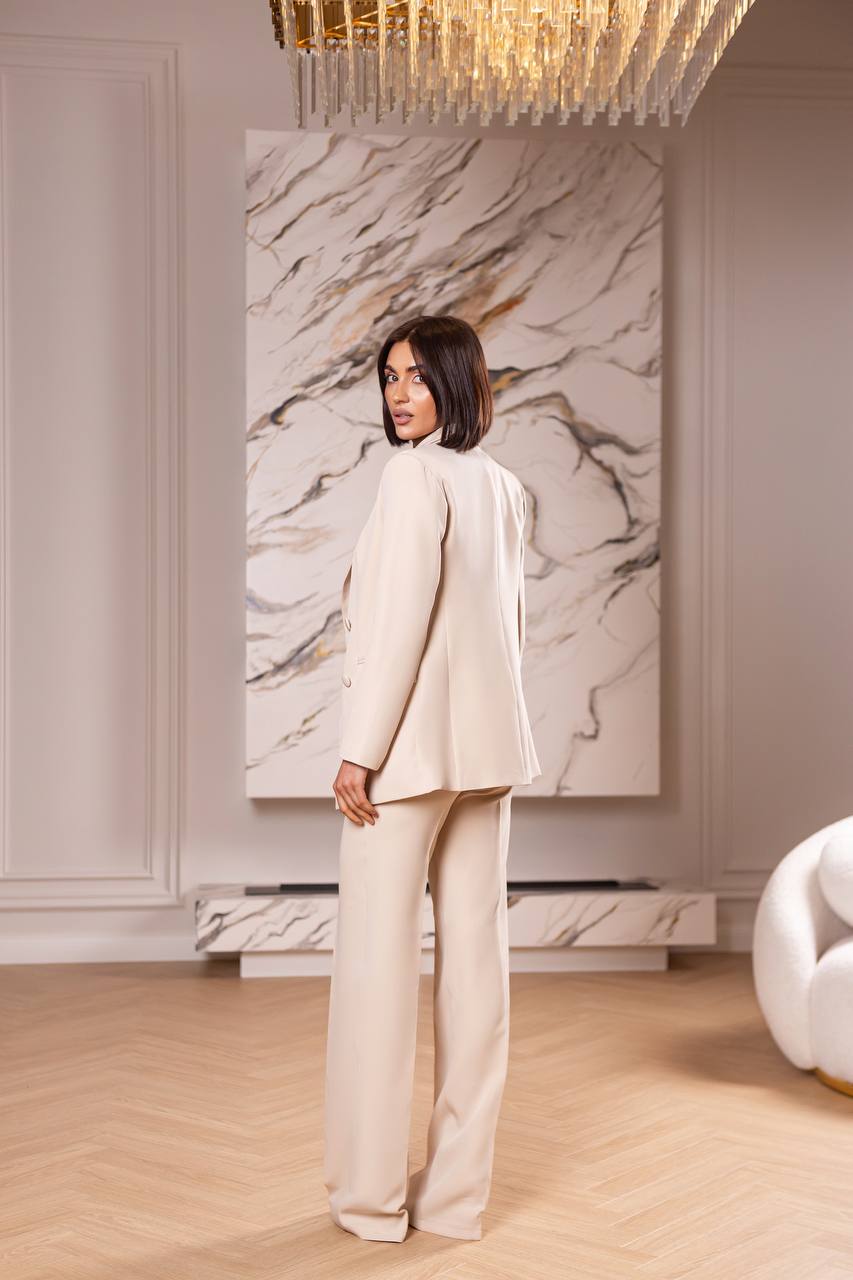 Woman in a beige suit standing in a stylish room with marble wall art and modern decor.