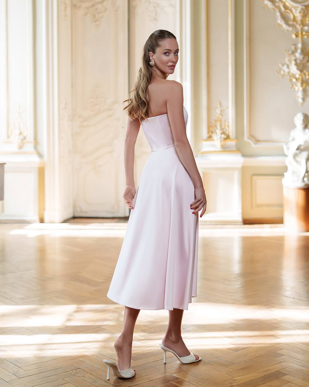 Woman in a white strapless dress standing in a bright, elegant room.