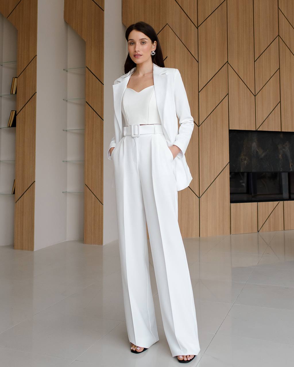 Woman in a white suit standing in a modern interior setting with wooden walls.
