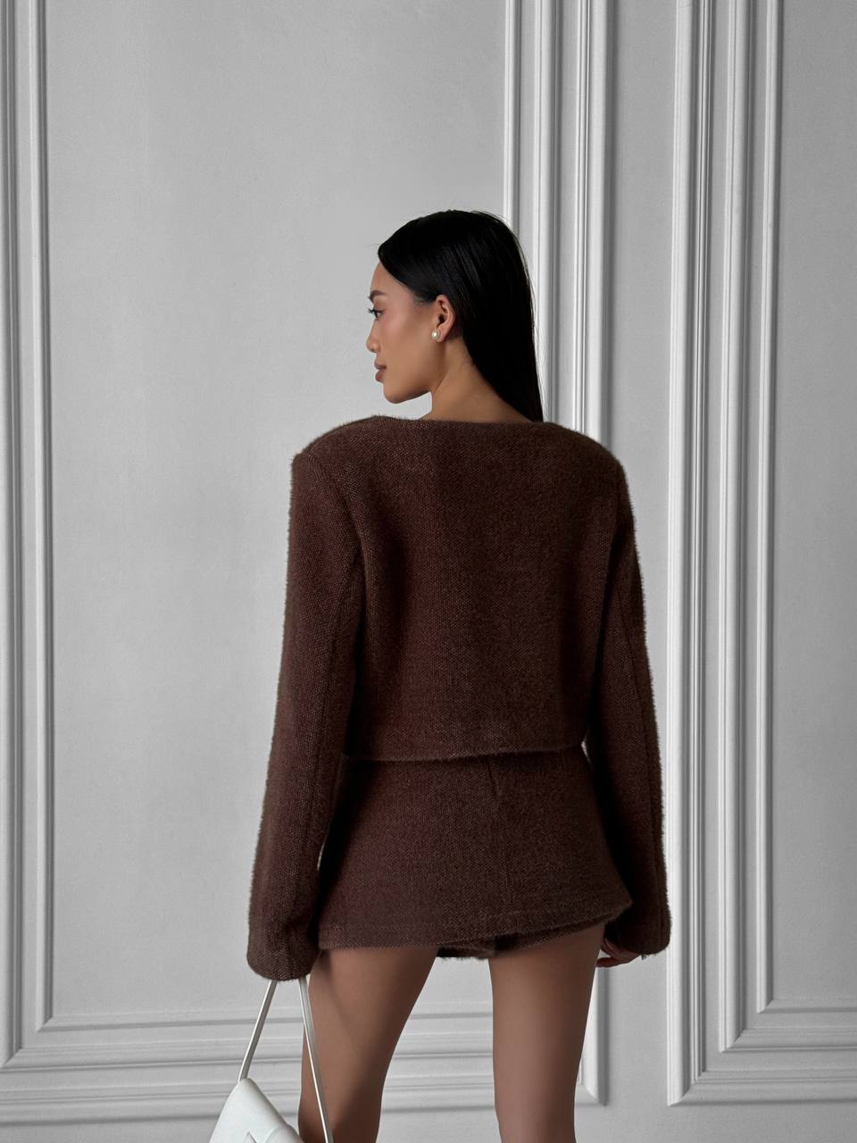 Woman wearing a brown textured jacket against a gray paneled wall