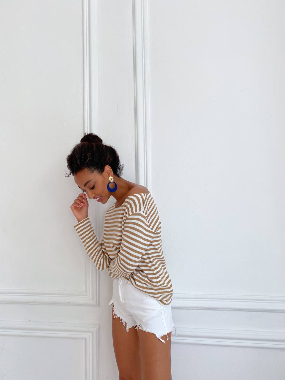 Woman wearing a striped sweater and white shorts against a white wall