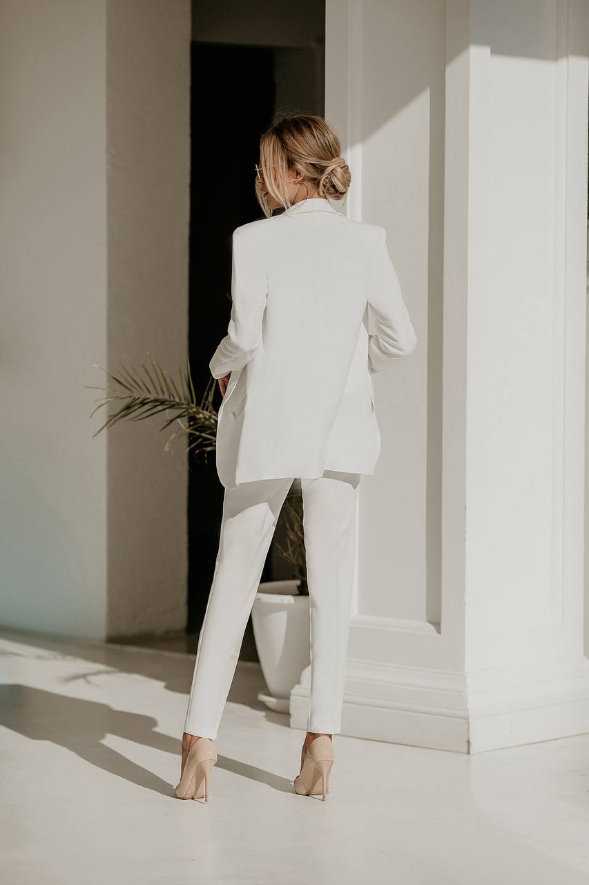 Woman in a white suit standing in a minimalistic room with a plant.