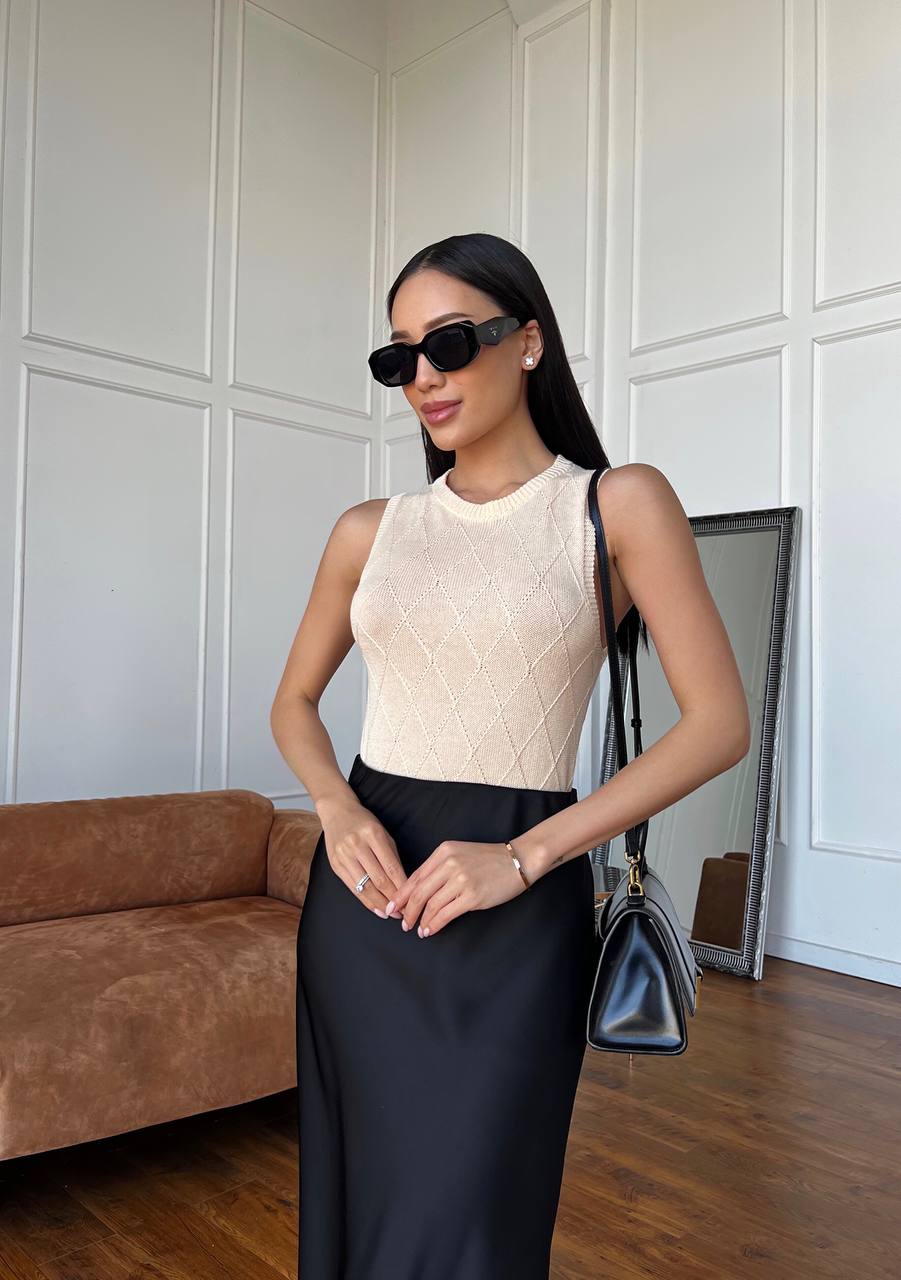 Woman in a stylish outfit with a cream top and black skirt, holding a blue handbag indoors.