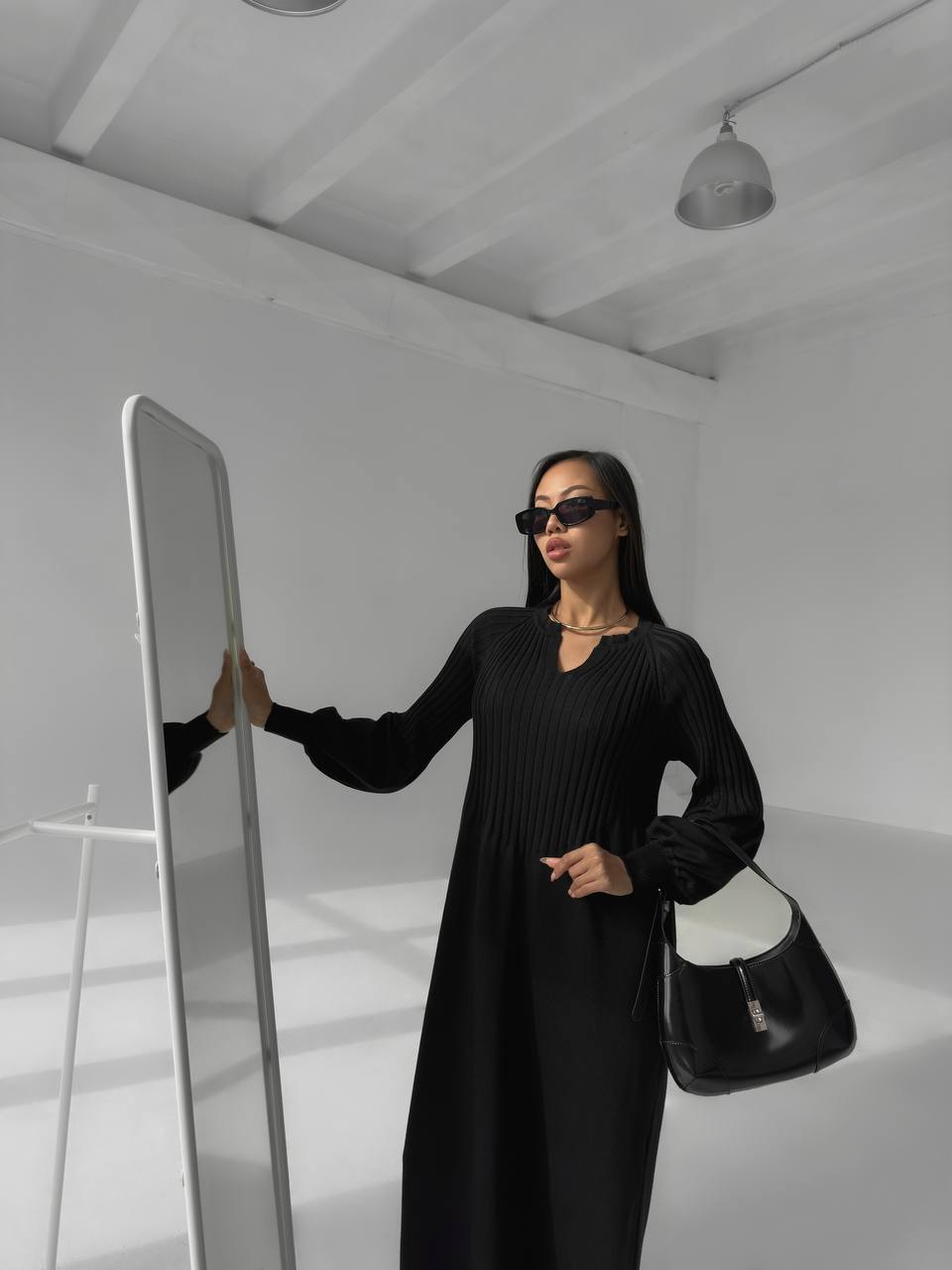 Woman in a black outfit holding a mirror in a minimalistic setting