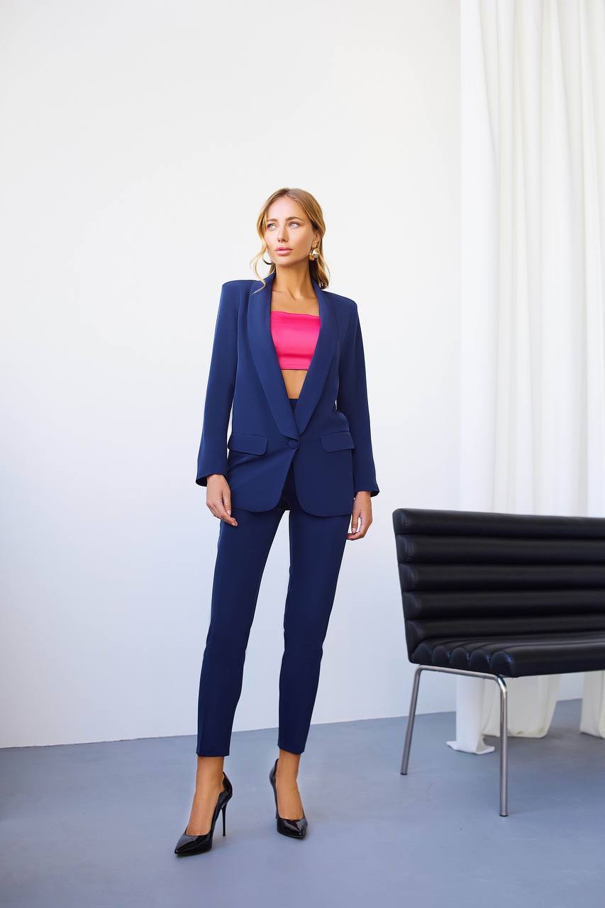 Woman in a blue suit standing in a minimalistic room with a black chair.