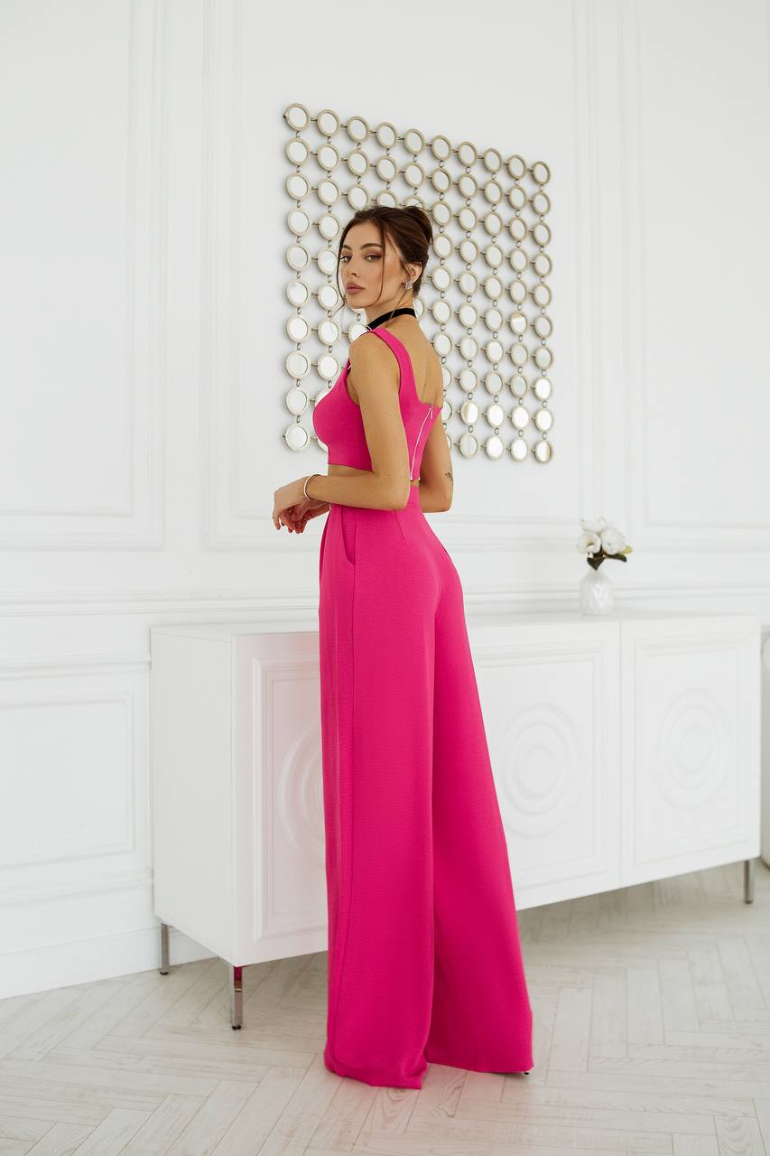 Woman in a bright pink jumpsuit standing in a room with a decorative wall.