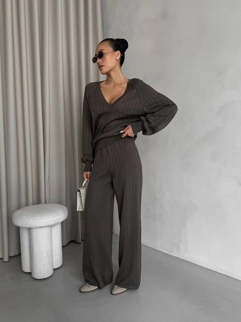 Woman in a dark gray outfit standing against a neutral background