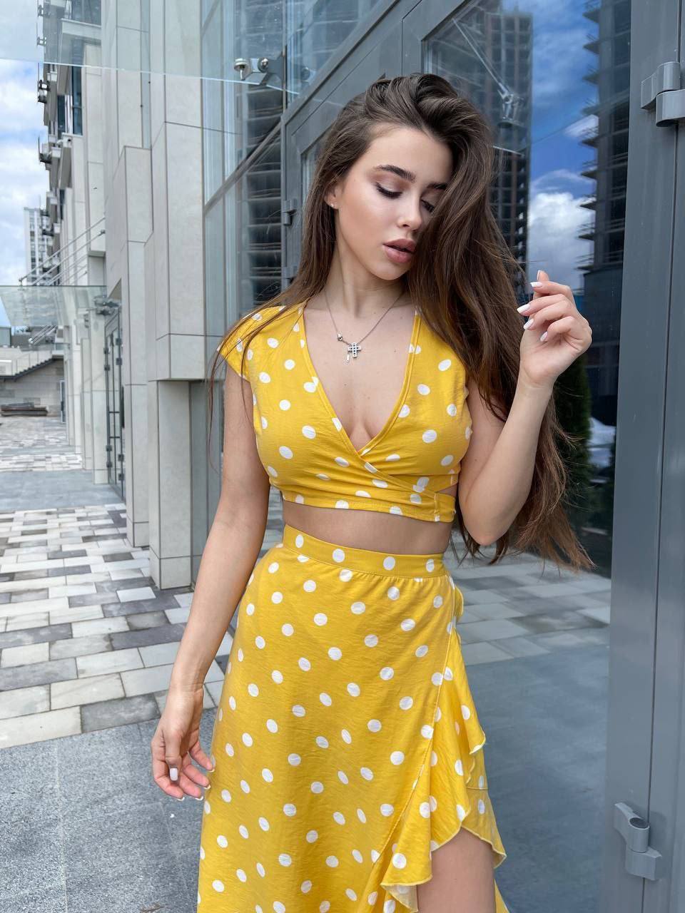 Woman in a yellow polka dot dress standing outdoors with modern architecture in the background