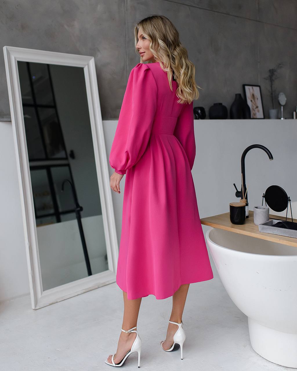 Woman in a bright pink dress standing in a modern bathroom.